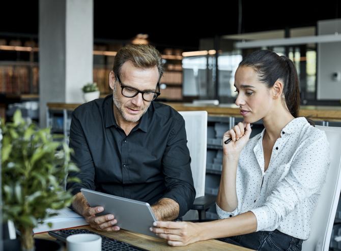 Two people sitting in an office looking at a tablet together