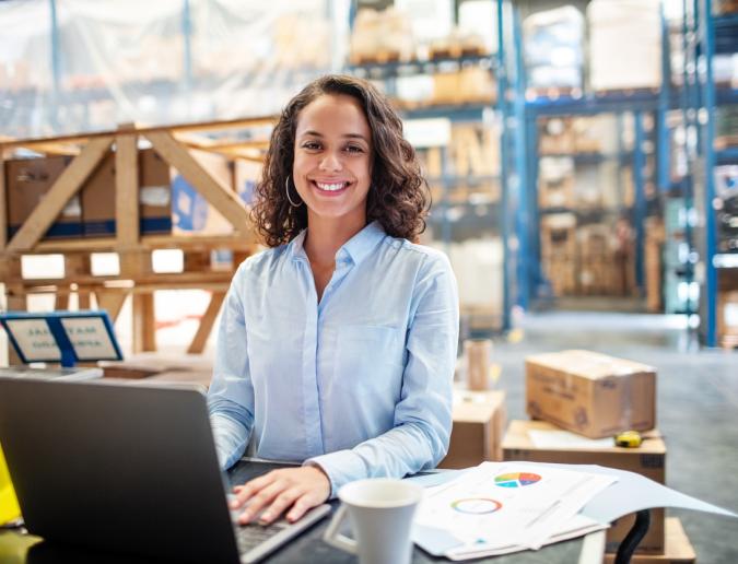 Business woman working on laptop at a warehouse.